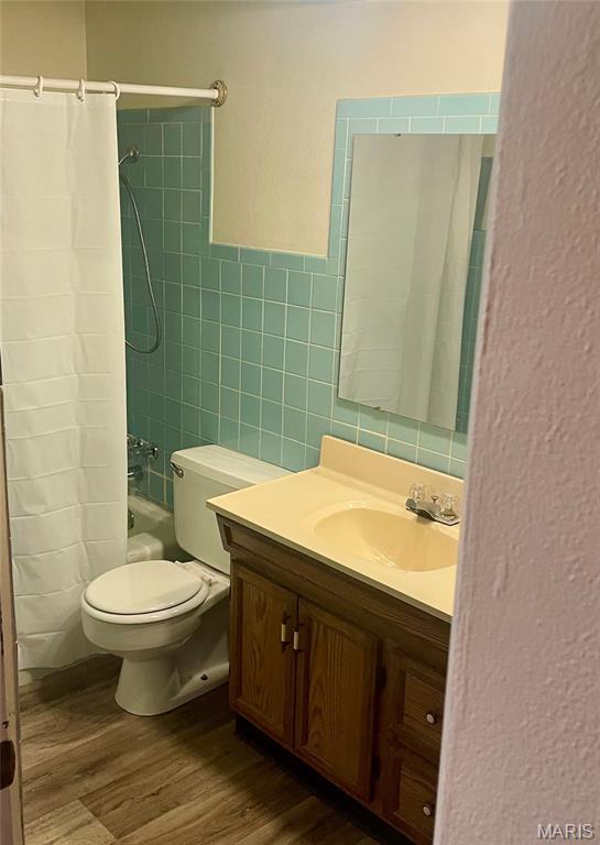 76 Cheshire Dr, Belleville, IL 62223 - full bathroom featuring wood finished floors, vanity, tile walls, shower / tub combo with curtain, and a wainscoted wall