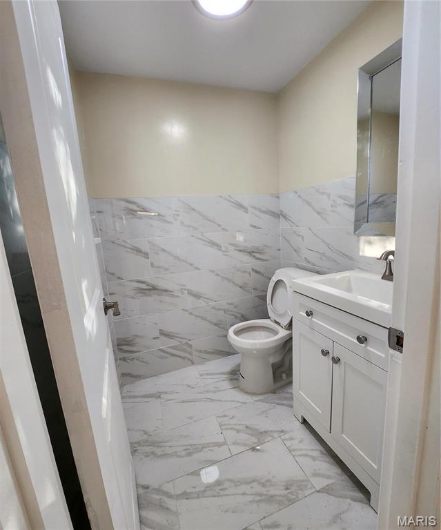 2020 S Brentwood Blvd, Saint Louis, MO 63144 - half bathroom featuring tile walls, vanity, marble finish floors, and a wainscoted wall