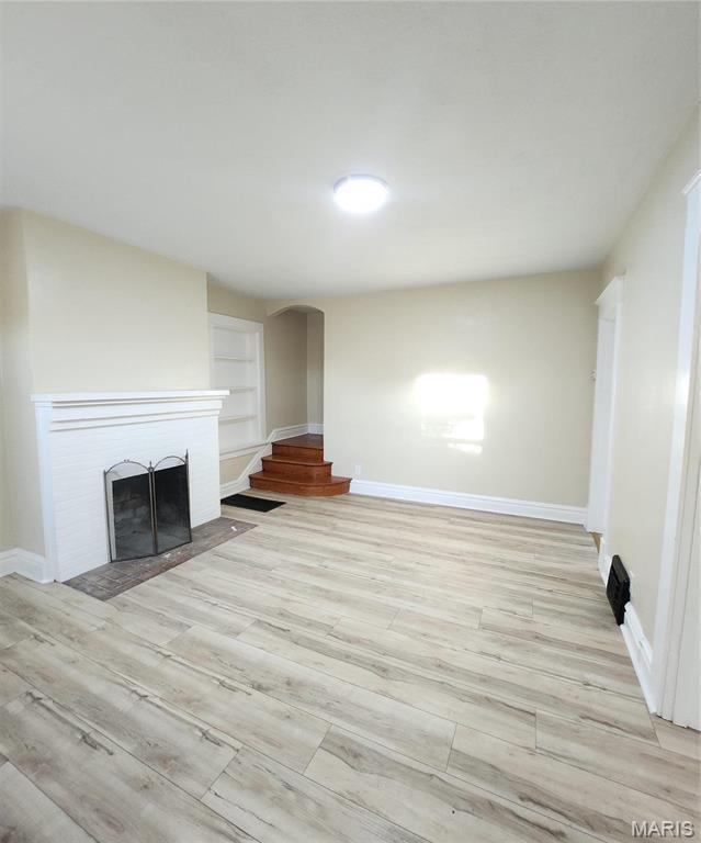 2020 S Brentwood Blvd, Saint Louis, MO 63144 - unfurnished living room with arched walkways, a fireplace, and light wood-style floors