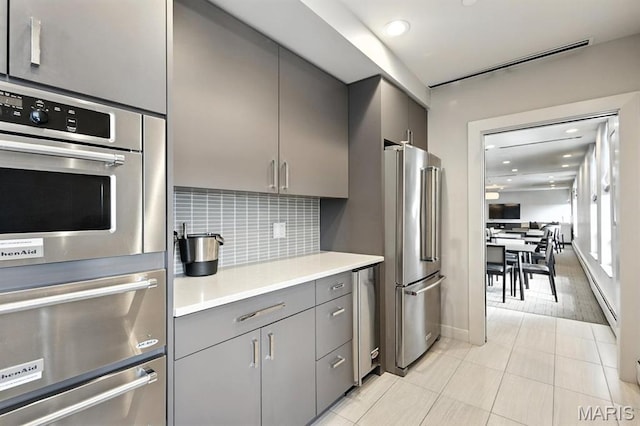 200 S Brentwood Blvd Unit 15C, Clayton, MO 63105 - kitchen featuring appliances with stainless steel finishes, gray cabinets, a warming drawer, light countertops, and backsplash