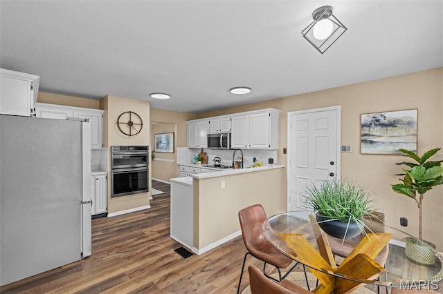 17 Beaujolais Dr, Florissant, MO 63031 - kitchen featuring appliances with stainless steel finishes, a peninsula, light countertops, wood finished floors, and white cabinets