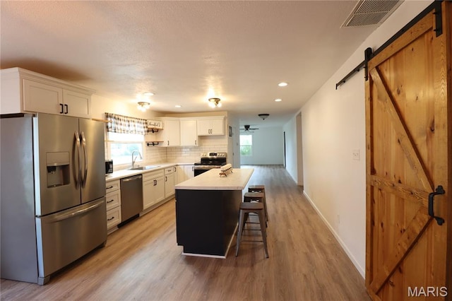 1001 E 2nd St, Saint Peter, IL 62880 - kitchen featuring stainless steel appliances, a barn door, light wood-style flooring, light countertops, and white cabinetry