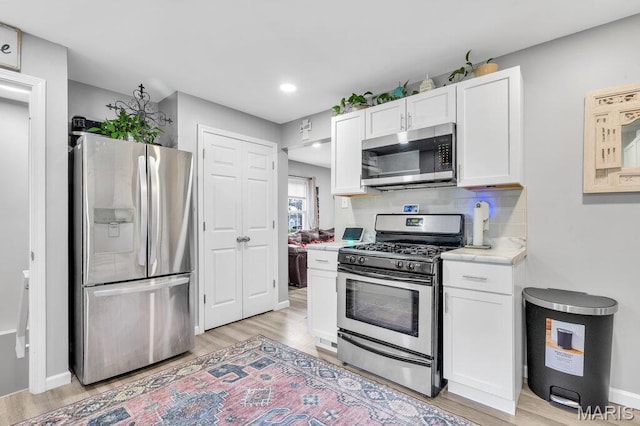 3711 Ashby Rd, Saint Ann, MO 63074 - kitchen with stainless steel appliances, white cabinets, light countertops, light wood-style flooring, and decorative backsplash