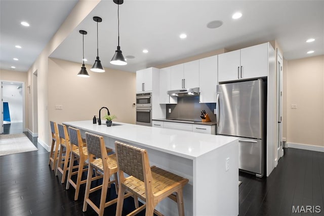 5951 Jamieson Ave, Saint Louis, MO 63109 - kitchen with appliances with stainless steel finishes, under cabinet range hood, dark wood-type flooring, white cabinetry, and a kitchen island with sink