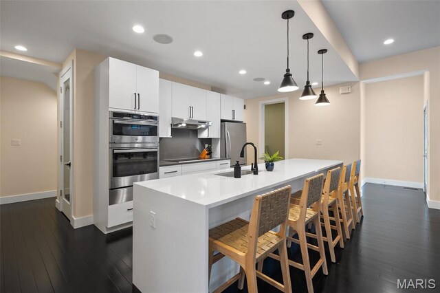 5951 Jamieson Ave, Saint Louis, MO 63109 - kitchen with stainless steel appliances, under cabinet range hood, dark wood finished floors, recessed lighting, and a kitchen breakfast bar