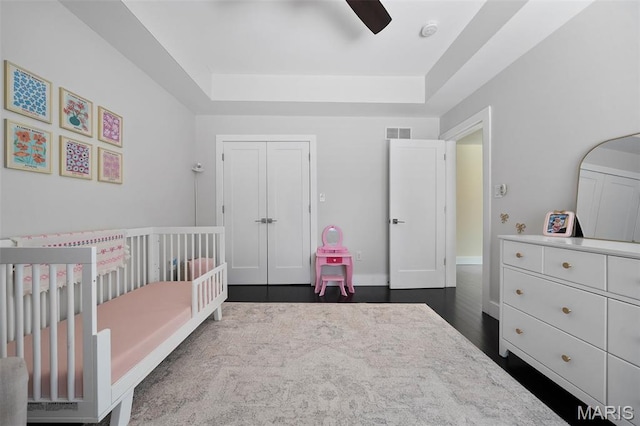 5951 Jamieson Ave, Saint Louis, MO 63109 - bedroom with a tray ceiling, a crib, a closet, a ceiling fan, and dark wood-type flooring