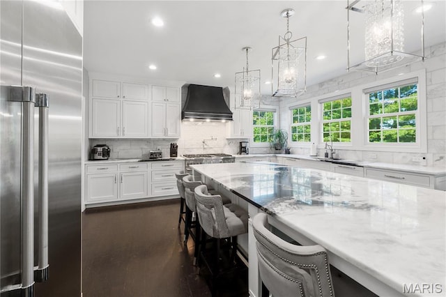 12429 Nicholas Ln, Saint Louis, MO 63131 - kitchen featuring stainless steel built in refrigerator, custom range hood, decorative backsplash, light stone countertops, and recessed lighting
