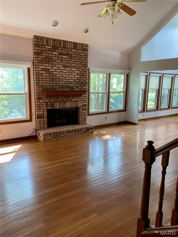 12020 Jacobson Ct, Saint Louis, MO 63044 - unfurnished living room featuring a ceiling fan, wood finished floors, a fireplace, and vaulted ceiling