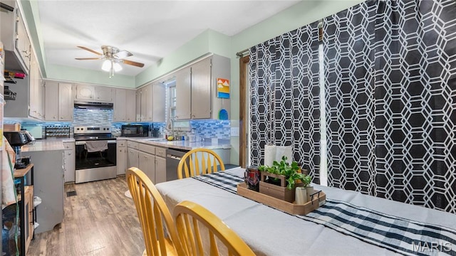 19954 Ironwood Ln, Lebanon, MO 65536 - kitchen featuring stainless steel appliances, under cabinet range hood, a ceiling fan, light wood-style floors, and decorative backsplash