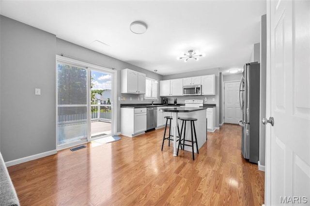 2330 Eagle Pines Dr, Saint Charles, MO 63303 - kitchen featuring appliances with stainless steel finishes, dark countertops, white cabinetry, a kitchen bar, and a kitchen island