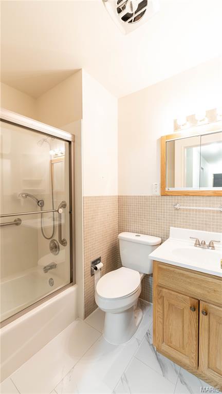 2480 Cambridge Dr, Florissant, MO 63033 - full bathroom with combined bath / shower with glass door, vanity, marble look tile flooring, a wainscoted wall, and tile walls