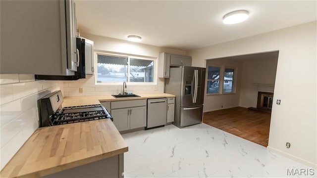 2480 Cambridge Dr, Florissant, MO 63033 - kitchen featuring stainless steel appliances, butcher block counters, a glass covered fireplace, gray cabinets, and decorative backsplash