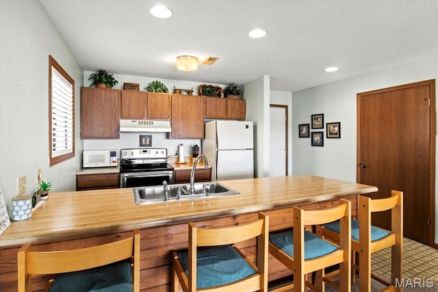 40 Robinwood Unit 2C, Lake Ozark, MO 65049 - kitchen featuring white appliances, under cabinet range hood, a breakfast bar, brown cabinetry, and light countertops