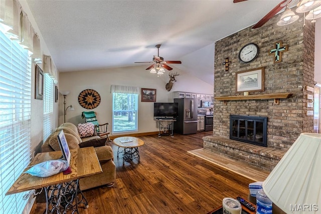 living area featuring ceiling fan, wood finished floors, vaulted ceiling, and a brick fireplace