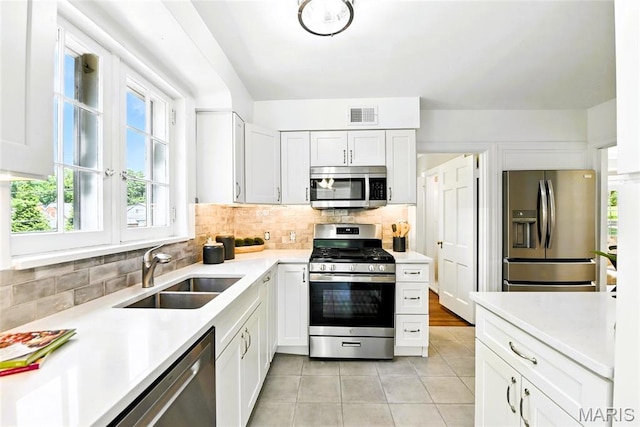 8049 Gannon Ave, Saint Louis, MO 63130 - kitchen featuring stainless steel appliances, light tile patterned floors, backsplash, light countertops, and white cabinets