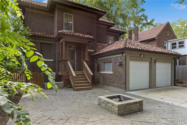 316 Melville Ave, University City, MO 63130 - mediterranean / spanish home featuring a tile roof, brick siding, an attached garage, an outdoor fire pit, and concrete driveway
