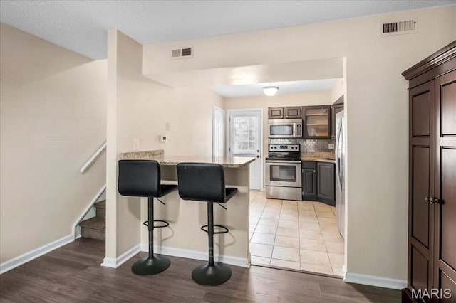 9053 W Swan Cir, Brentwood, MO 63144 - kitchen with stainless steel appliances, a peninsula, a kitchen breakfast bar, light wood-style floors, and backsplash