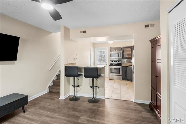 9053 W Swan Cir, Brentwood, MO 63144 - kitchen with appliances with stainless steel finishes, a breakfast bar, a peninsula, light wood-type flooring, and ceiling fan