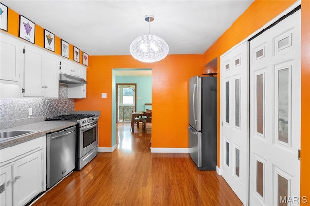 1239 Vero Ln, Ellisville, MO 63011 - kitchen with appliances with stainless steel finishes, a chandelier, white cabinetry, wood finished floors, and tasteful backsplash