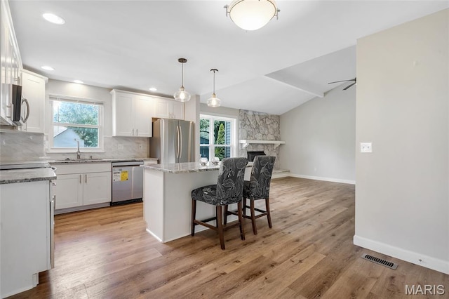 904 Ampere Pl, Lake St Louis, MO 63367 - kitchen with appliances with stainless steel finishes, decorative backsplash, a kitchen island, white cabinetry, and a kitchen breakfast bar