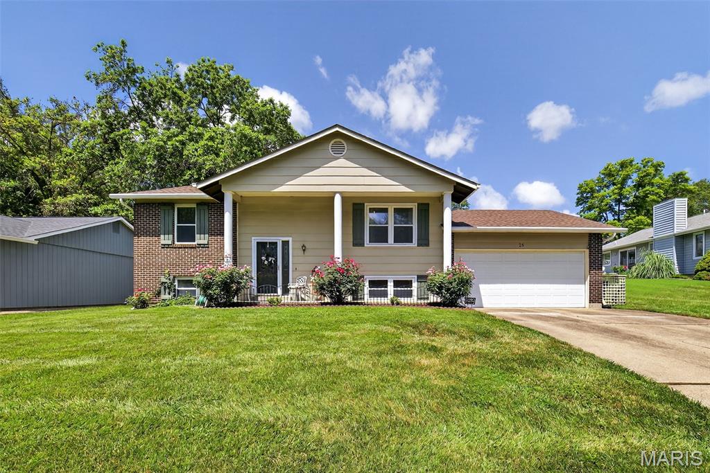 25 Universal Dr, Saint Peters, MO 63376 - raised ranch featuring brick siding, an attached garage, a front yard, driveway, and a porch
