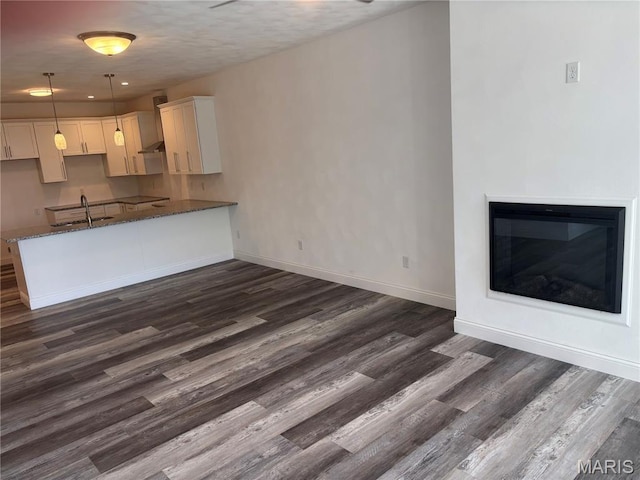 314 Captains Ct, Grafton, IL 62037 - kitchen with dark stone countertops, dark wood-type flooring, white cabinetry, wall chimney range hood, and a glass covered fireplace