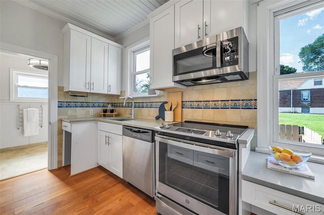 2733 Hermitage Ave, Saint Louis, MO 63143 - kitchen featuring stainless steel appliances, ornamental molding, light wood-style flooring, white cabinets, and tasteful backsplash