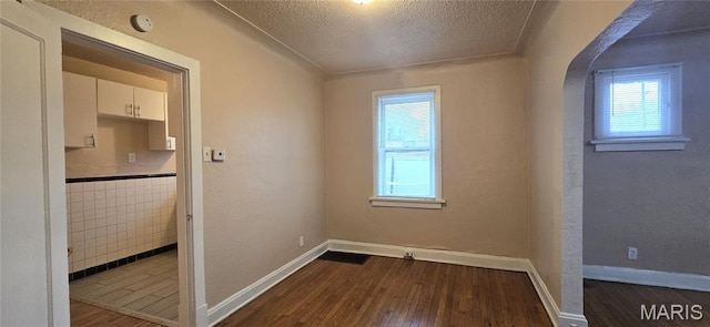 6128 Bircher St, Saint Louis, MO 63120 - empty room featuring healthy amount of natural light, dark wood-style floors, a textured ceiling, arched walkways, and a smoke detector