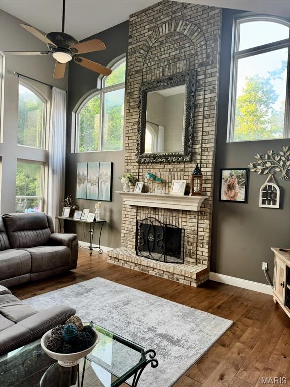 616 Remmick Stables Ct, Ofallon, MO 63368 - living area featuring a brick fireplace, a ceiling fan, a towering ceiling, and wood finished floors