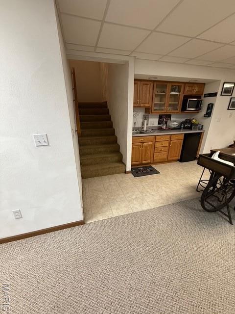 130 Regency Pl, Millstadt, IL 62260 - kitchen featuring stainless steel microwave, brown cabinets, a paneled ceiling, glass insert cabinets, and light colored carpet