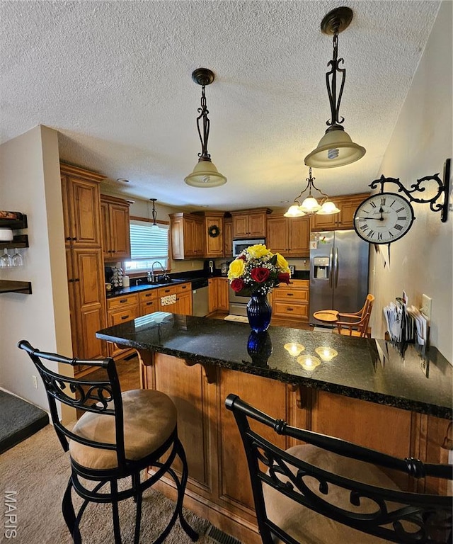 22 Settlers Trl, Hannibal, MO 63401 - kitchen featuring appliances with stainless steel finishes, brown cabinets, a kitchen bar, a textured ceiling, and hanging light fixtures