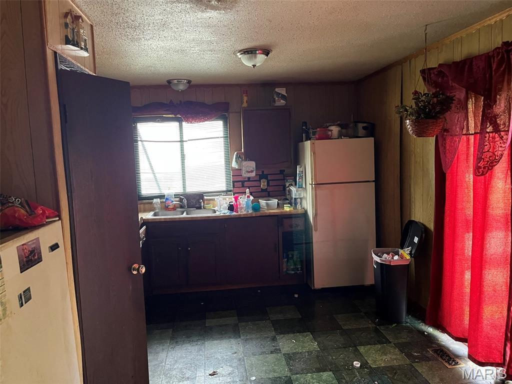 2345 Derhake Rd, Florissant, MO 63033 - kitchen featuring freestanding refrigerator, a textured ceiling, fridge, wooden walls, and dark floors