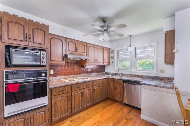 7373 Marwinette Ave, Saint Louis, MO 63116 - kitchen featuring stainless steel appliances, under cabinet range hood, light wood-type flooring, brown cabinets, and decorative backsplash