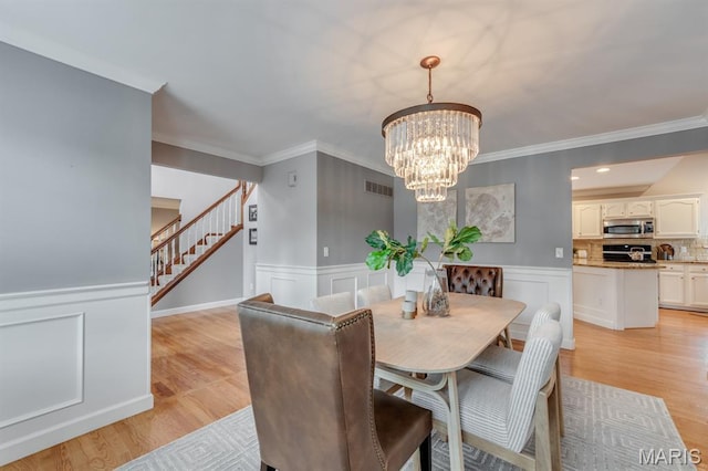 13153 Barrett Meadows Dr, Ballwin, MO 63021 - dining room with stairway, a chandelier, ornamental molding, a wainscoted wall, and light wood-type flooring