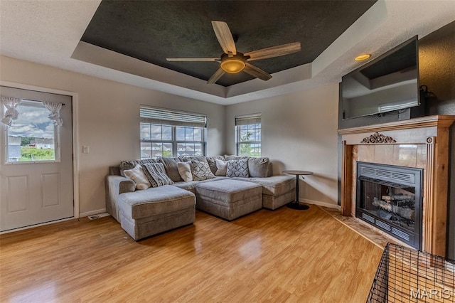 143 Lyle Curtis Cir, Waynesville, MO 65583 - living room featuring a tray ceiling, a tile fireplace, light wood-style flooring, and ceiling fan