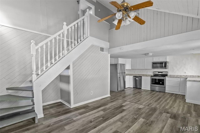 2826 Dawnview Dr, Florissant, MO 63031 - unfurnished living room with dark wood-style flooring, wood walls, stairway, ceiling fan, and high vaulted ceiling