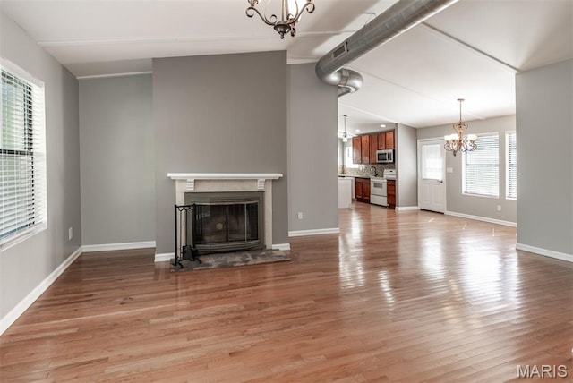 1409 Castle Mill Dr, Arnold, MO 63010 - unfurnished living room featuring a chandelier, a glass covered fireplace, and light wood-type flooring