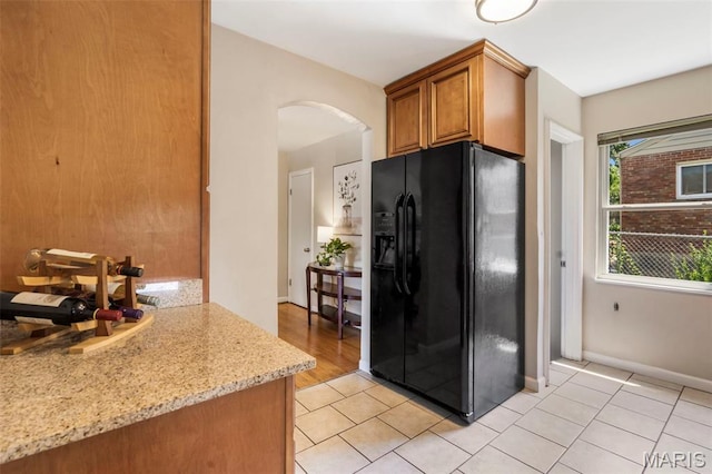 346 Madison Ave, Saint Louis, MO 63119 - kitchen featuring black fridge with ice dispenser, arched walkways, light stone counters, light tile patterned floors, and brown cabinetry