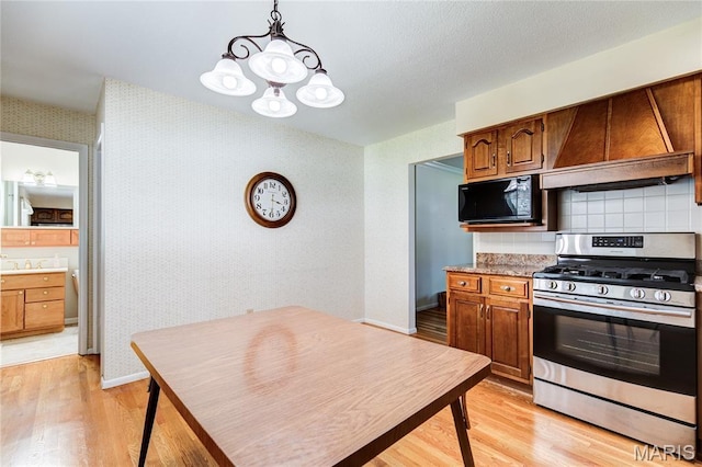 4828 Plum Tree Ln, Hazelwood, MO 63042 - kitchen with gas stove, black microwave, wallpapered walls, light wood-style flooring, and a chandelier