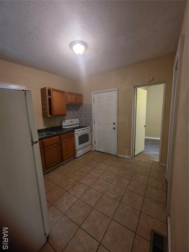 3421 Belt Ave, Saint Louis, MO 63120 - kitchen featuring white appliances, a textured ceiling, light tile patterned floors, dark countertops, and brown cabinetry