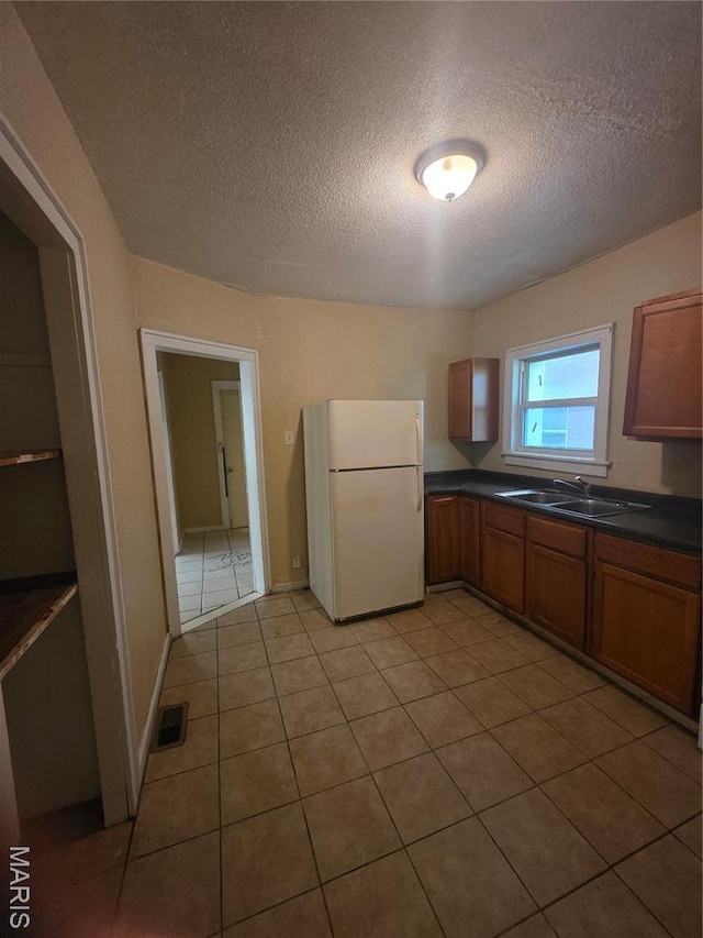 3421 Belt Ave, Saint Louis, MO 63120 - kitchen featuring freestanding refrigerator, a textured ceiling, dark countertops, brown cabinetry, and light tile patterned floors