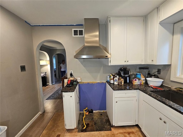 2060 Washington St, Florissant, MO 63033 - kitchen featuring wall chimney exhaust hood, wood finished floors, white cabinets, arched walkways, and dark stone countertops