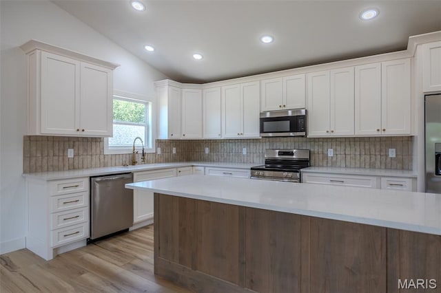 1817 Vadie Ave, Lebanon, MO 65536 - kitchen featuring stainless steel appliances, vaulted ceiling, white cabinetry, decorative backsplash, and light wood-style floors