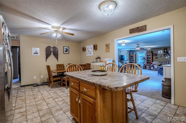 30053 Emily Ln, Lebanon, MO 65536 - kitchen featuring a ceiling fan, a kitchen bar, brown cabinets, a kitchen island, and light stone finish flooring