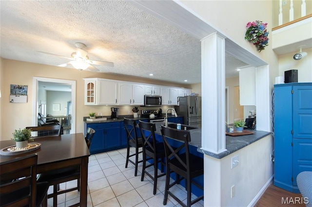 11907 Pine Forest Dr, Rolla, MO 65401 - kitchen with stainless steel appliances, dark countertops, a breakfast bar area, white cabinets, and a textured ceiling