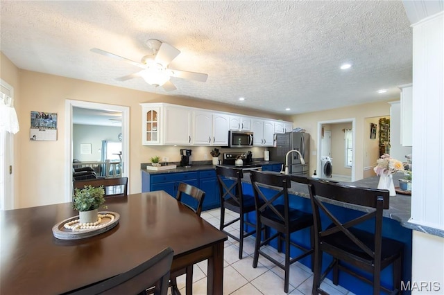 11907 Pine Forest Dr, Rolla, MO 65401 - kitchen with stainless steel appliances, dark countertops, light tile patterned floors, white cabinetry, and a kitchen breakfast bar