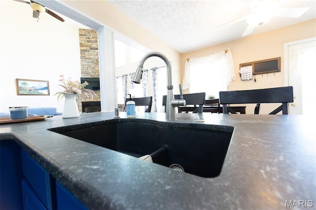 11907 Pine Forest Dr, Rolla, MO 65401 - kitchen with ceiling fan, a fireplace, healthy amount of natural light, a textured ceiling, and dark countertops