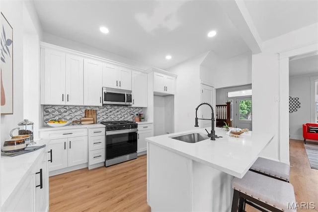 6206 Victoria Ave, Saint Louis, MO 63139 - kitchen with appliances with stainless steel finishes, light wood-style floors, white cabinetry, light countertops, and decorative backsplash