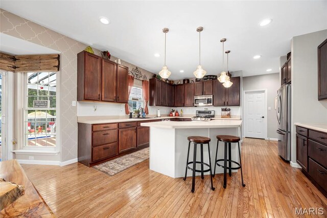 7742 Ardmore Dr, Ofallon, MO 63368 - kitchen with appliances with stainless steel finishes, light wood finished floors, a kitchen bar, light countertops, and a center island