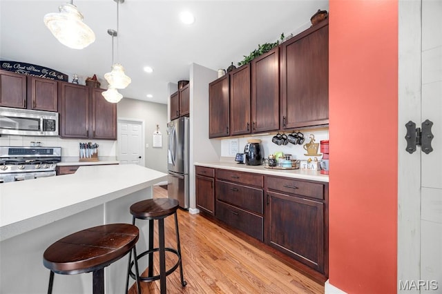 7742 Ardmore Dr, Ofallon, MO 63368 - kitchen with appliances with stainless steel finishes, light wood finished floors, light countertops, a kitchen bar, and decorative light fixtures
